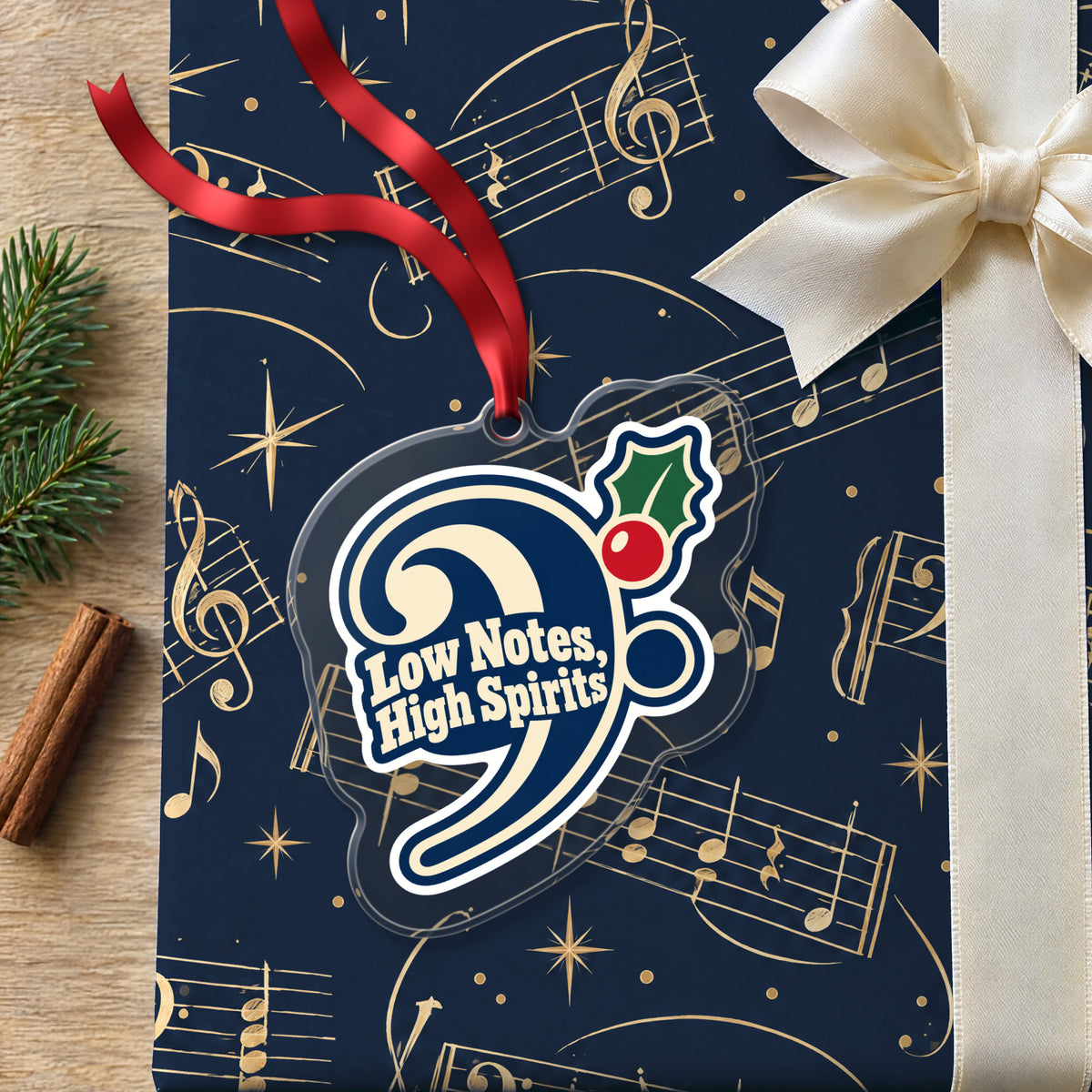 Low Notes, High Spirits Bass Clef clear acrylic Christmas ornament lying on a gift wrapped in Rhythm and Beat music wrapping paper