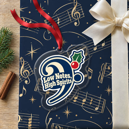 Low Notes, High Spirits Bass Clef clear acrylic Christmas ornament lying on a gift wrapped in Rhythm and Beat music wrapping paper
