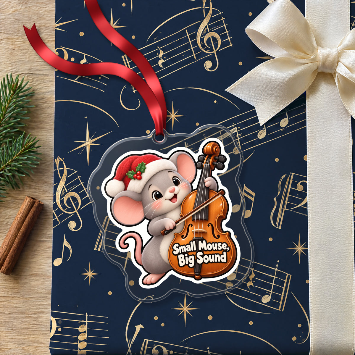 Small Mouse, Big Sound Cello clear acrylic Christmas ornament lying on a gift wrapped in Rhythm and Beat music wrapping paper