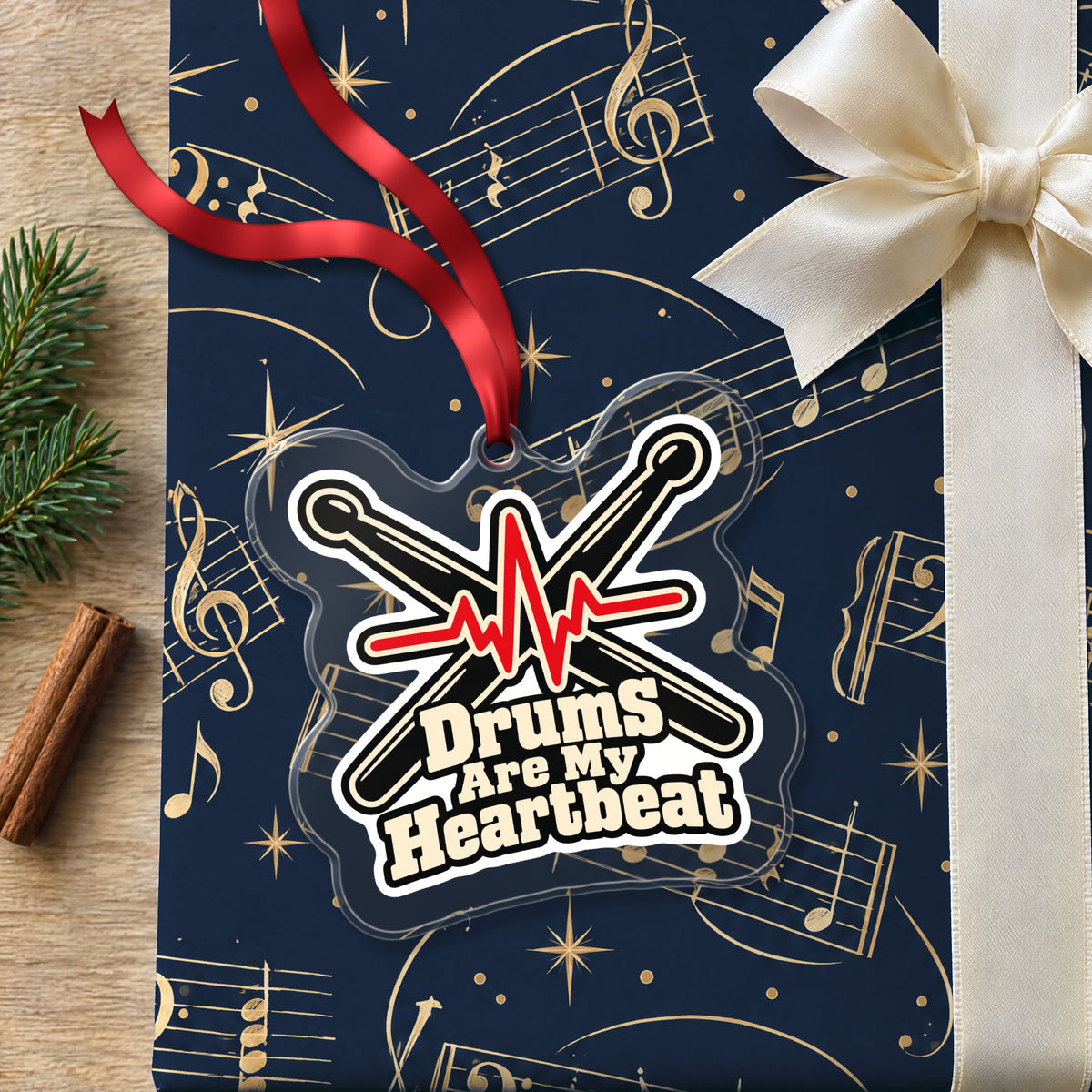 Drums Are My Heartbeat Drumsticks clear acrylic Christmas ornament lying on a gift wrapped in Rhythm and Beat music wrapping paper