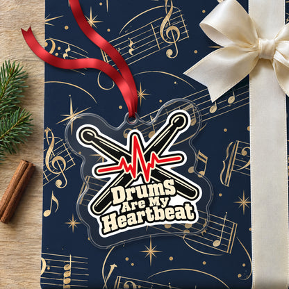 Drums Are My Heartbeat Drumsticks clear acrylic Christmas ornament lying on a gift wrapped in Rhythm and Beat music wrapping paper