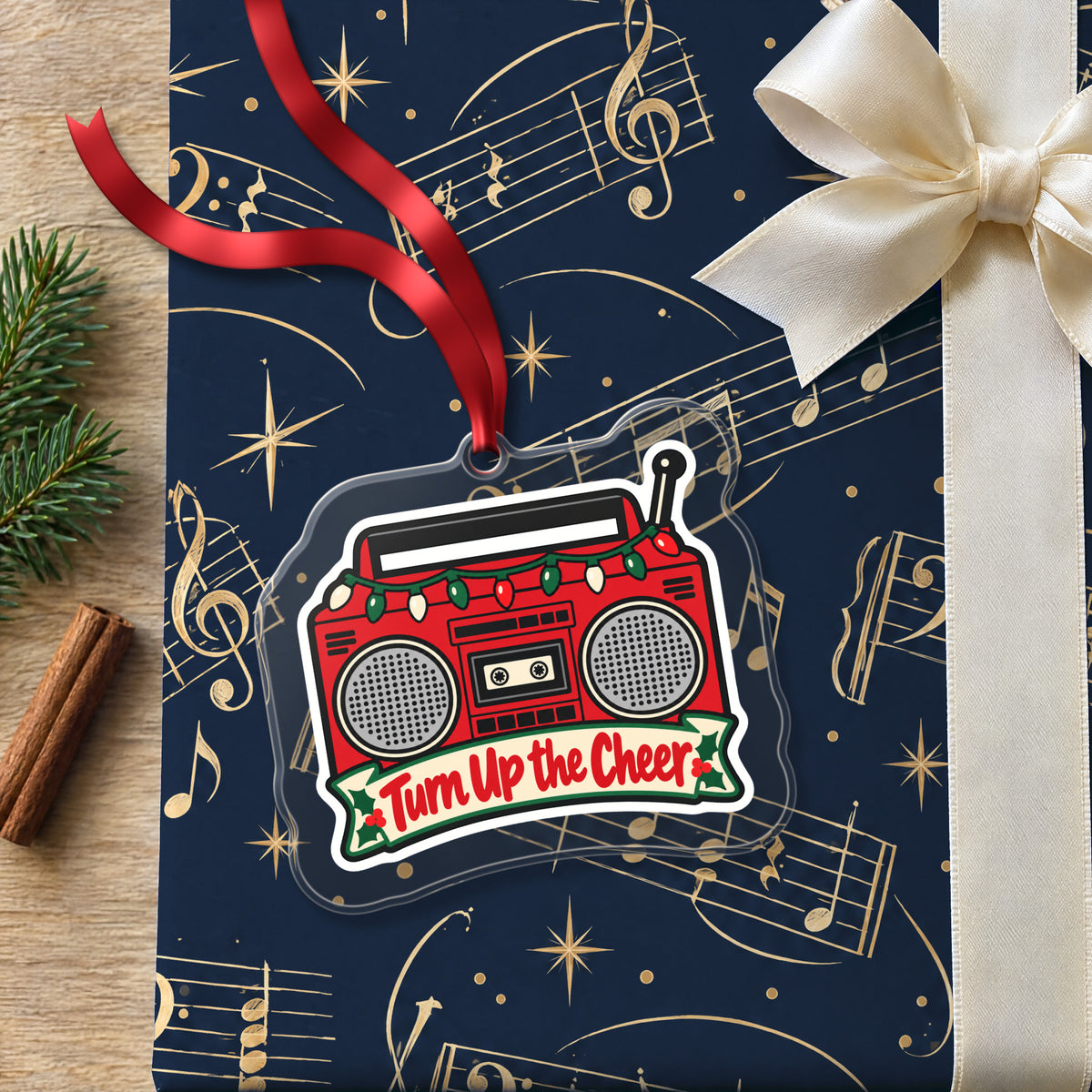 Turn Up the Cheer Boombox clear acrylic Christmas ornament lying on a gift wrapped in Rhythm and Beat music wrapping paper
