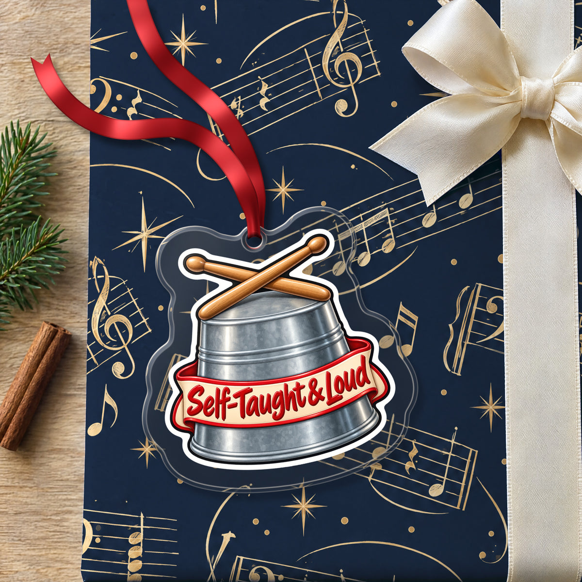 Self-Taught & Loud Bucket Drummer clear acrylic Christmas ornament lying on a gift wrapped in Rhythm and Beat music wrapping paper