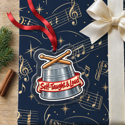 Self-Taught & Loud Bucket Drummer clear acrylic Christmas ornament lying on a gift wrapped in Rhythm and Beat music wrapping paper