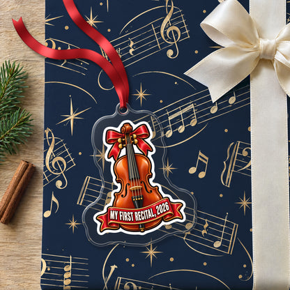 My First Violin Recital 2026 clear acrylic Christmas ornament lying on a gift wrapped in Rhythm and Beat music wrapping paper