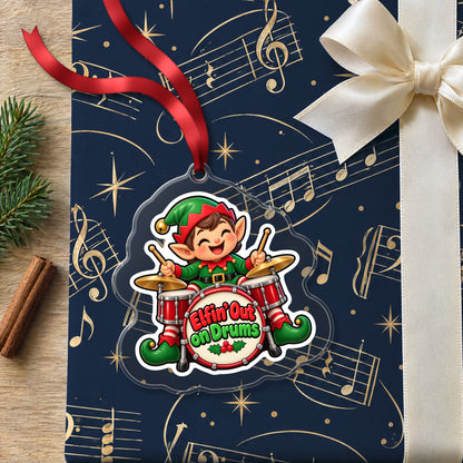 Elfin' Out on Drums Elf Drummer clear acrylic Christmas ornament lying on a gift wrapped in Rhythm and Beat music wrapping paper