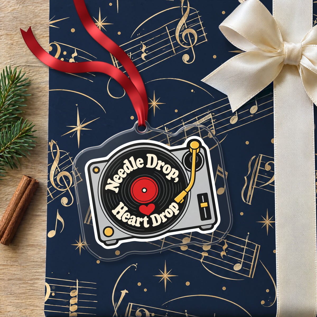 Needle Drop, Heart Drop Turntable clear acrylic Christmas ornament lying on a gift wrapped in Rhythm and Beat music wrapping paper
