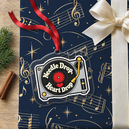 Needle Drop, Heart Drop Turntable clear acrylic Christmas ornament lying on a gift wrapped in Rhythm and Beat music wrapping paper