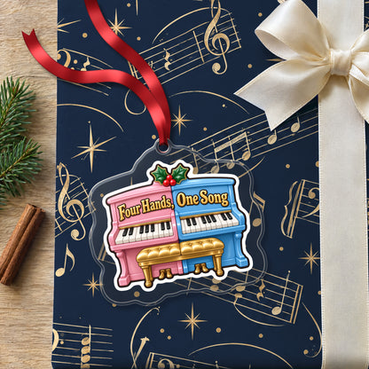 Four Hands, One Song Piano Duet clear acrylic Christmas ornament lying on a gift wrapped in Rhythm and Beat music wrapping paper