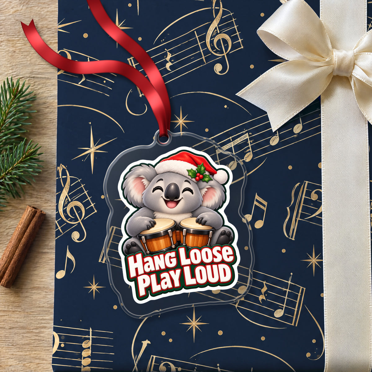 Hang Loose, Play Loud Koala Bongo clear acrylic Christmas ornament lying on a gift wrapped in Rhythm and Beat music wrapping paper