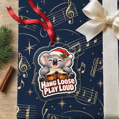 Hang Loose, Play Loud Koala Bongo clear acrylic Christmas ornament lying on a gift wrapped in Rhythm and Beat music wrapping paper