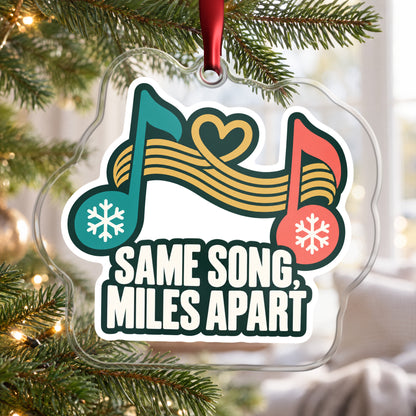 Same Song, Miles Apart Long Distance clear acrylic Christmas ornament hanging on a Christmas tree by a bright window