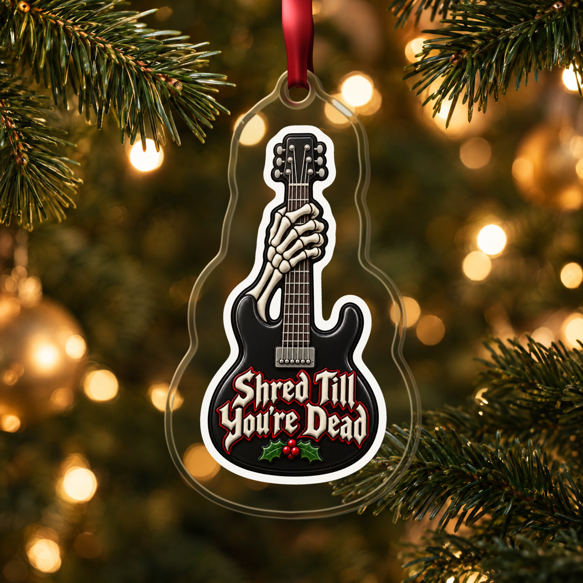Shred Till You're Dead Skeleton Guitar clear acrylic Christmas ornament hanging on a lit Christmas tree with warm gold lights