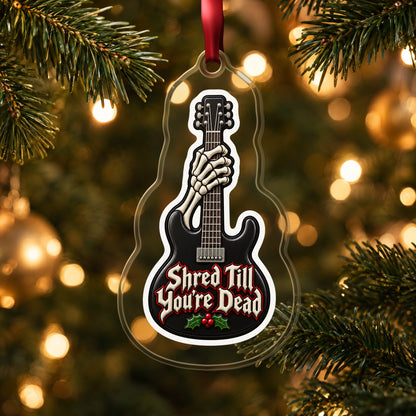 Shred Till You're Dead Skeleton Guitar clear acrylic Christmas ornament hanging on a lit Christmas tree with warm gold lights
