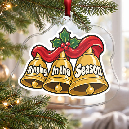 Ringing In the Season Handbells clear acrylic Christmas ornament hanging on a Christmas tree by a bright window