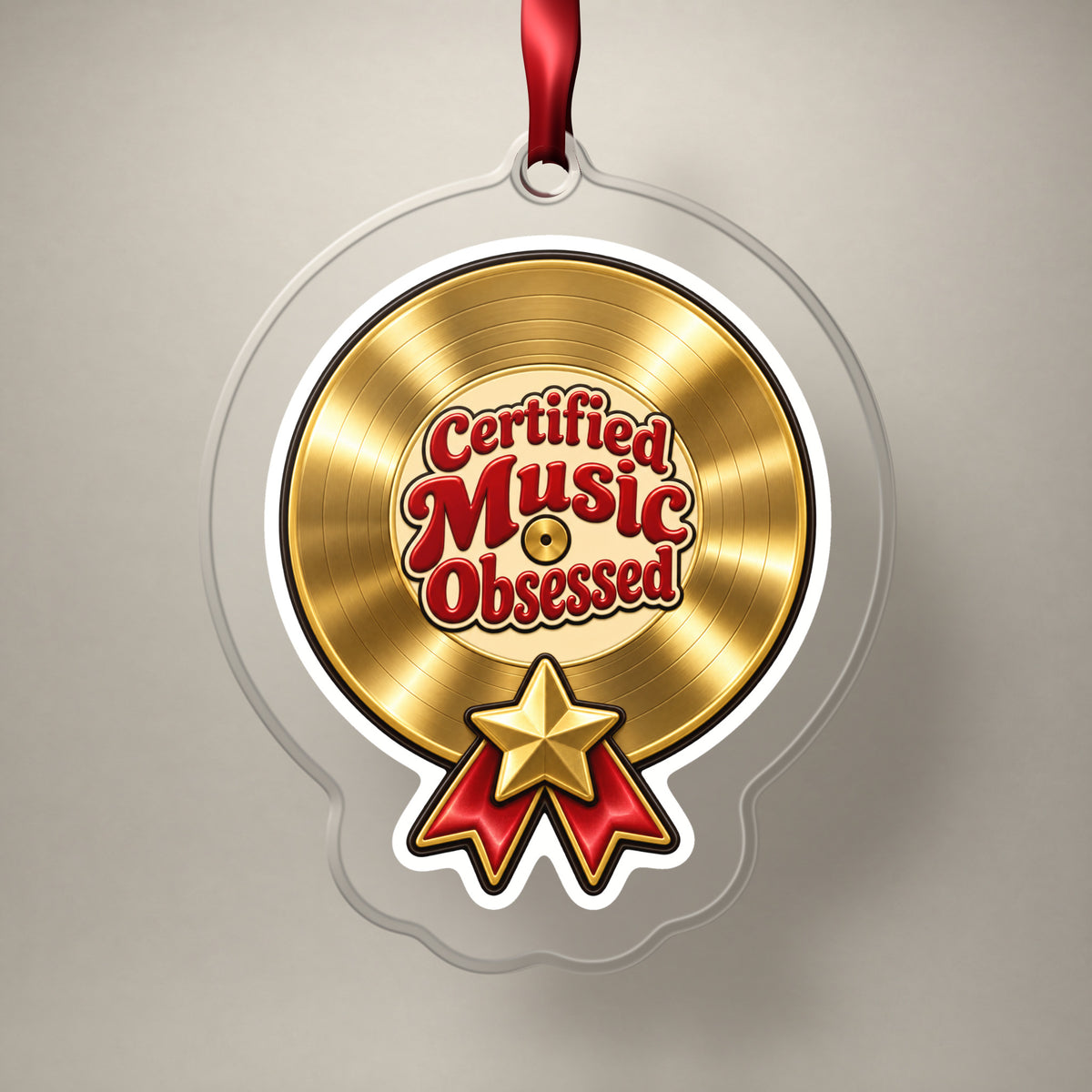 Certified Music Obsessed Gold Record clear acrylic Christmas ornament on a plain studio backdrop with its red ribbon