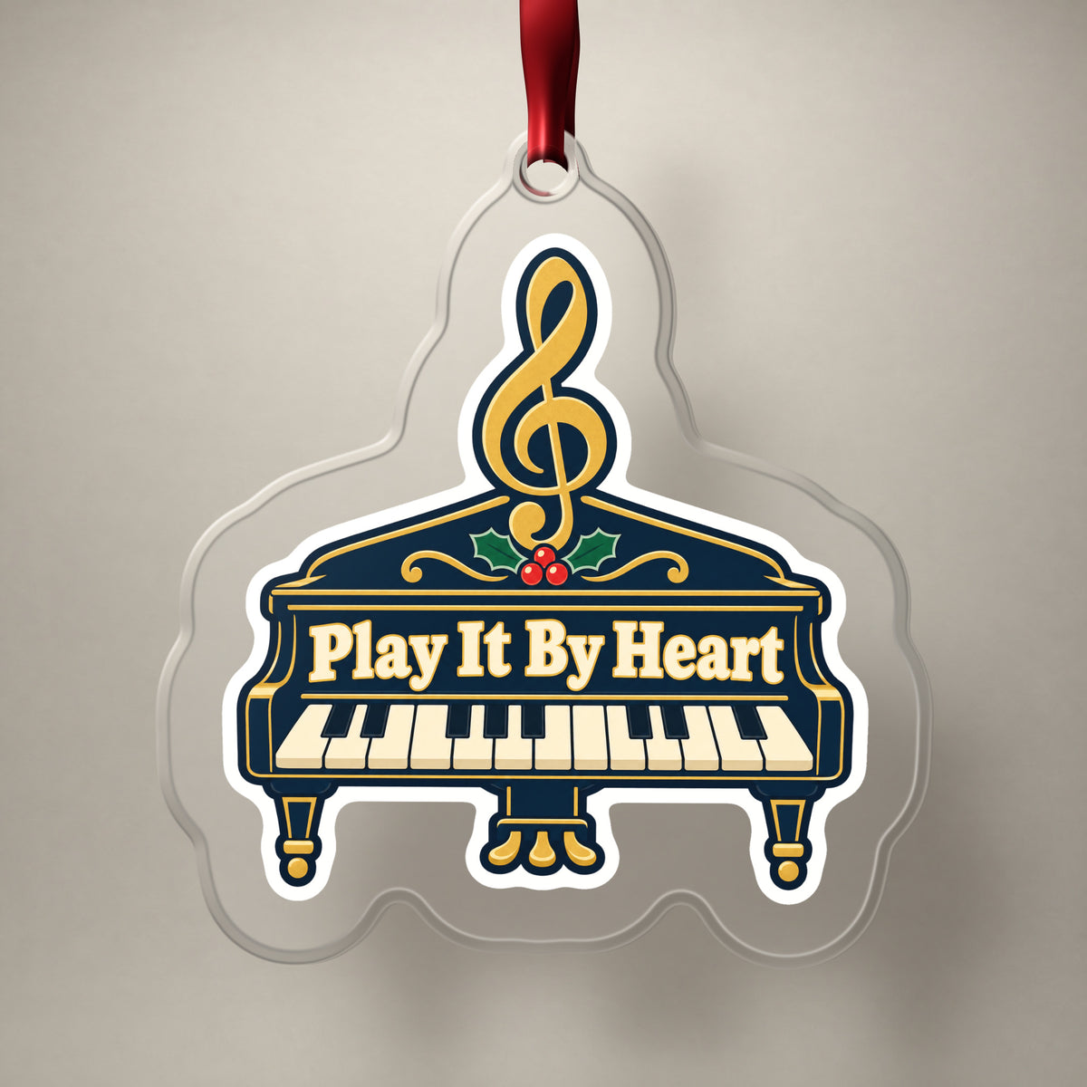 Play It By Heart Grand Piano clear acrylic Christmas ornament on a plain studio backdrop with its red ribbon