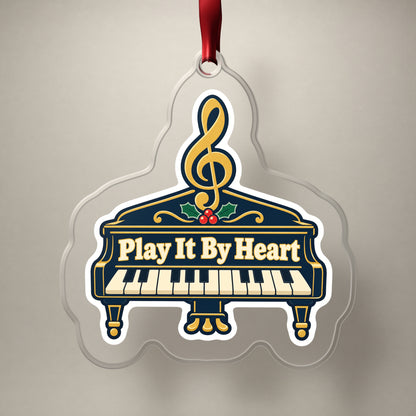 Play It By Heart Grand Piano clear acrylic Christmas ornament on a plain studio backdrop with its red ribbon