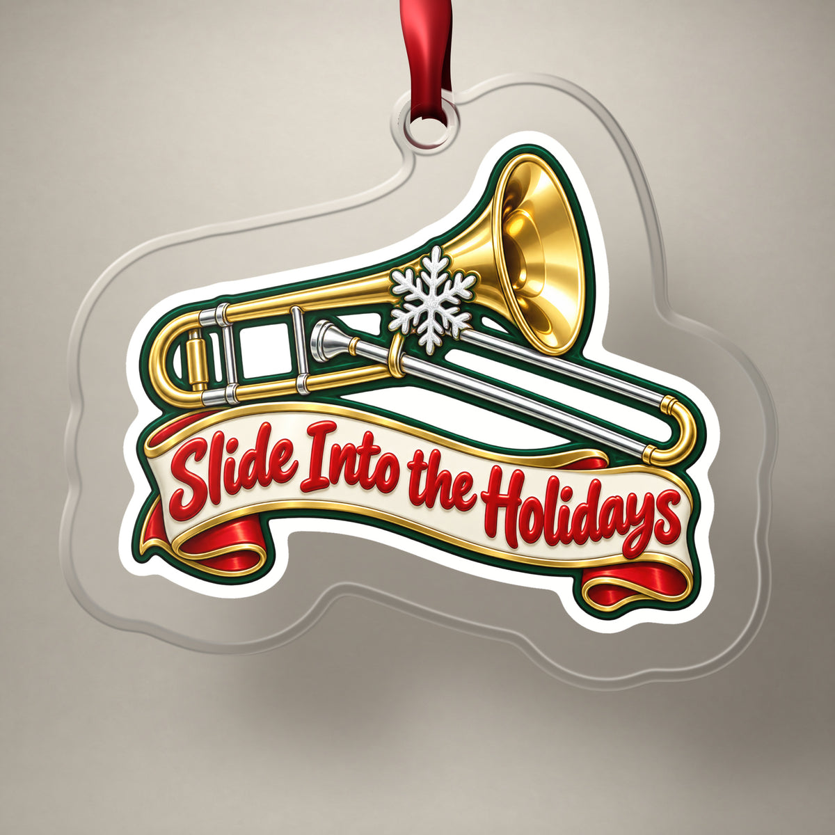 Slide Into the Holidays Trombone clear acrylic Christmas ornament on a plain studio backdrop with its red ribbon