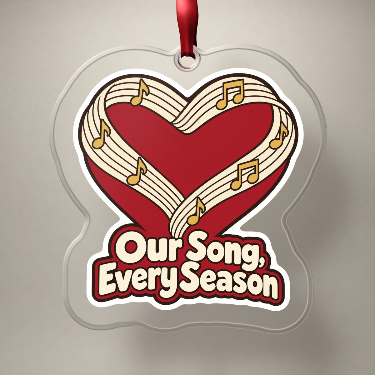 Our Song, Every Season Sheet Music Heart clear acrylic Christmas ornament on a plain studio backdrop with its red ribbon