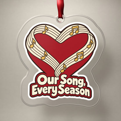 Our Song, Every Season Sheet Music Heart clear acrylic Christmas ornament on a plain studio backdrop with its red ribbon