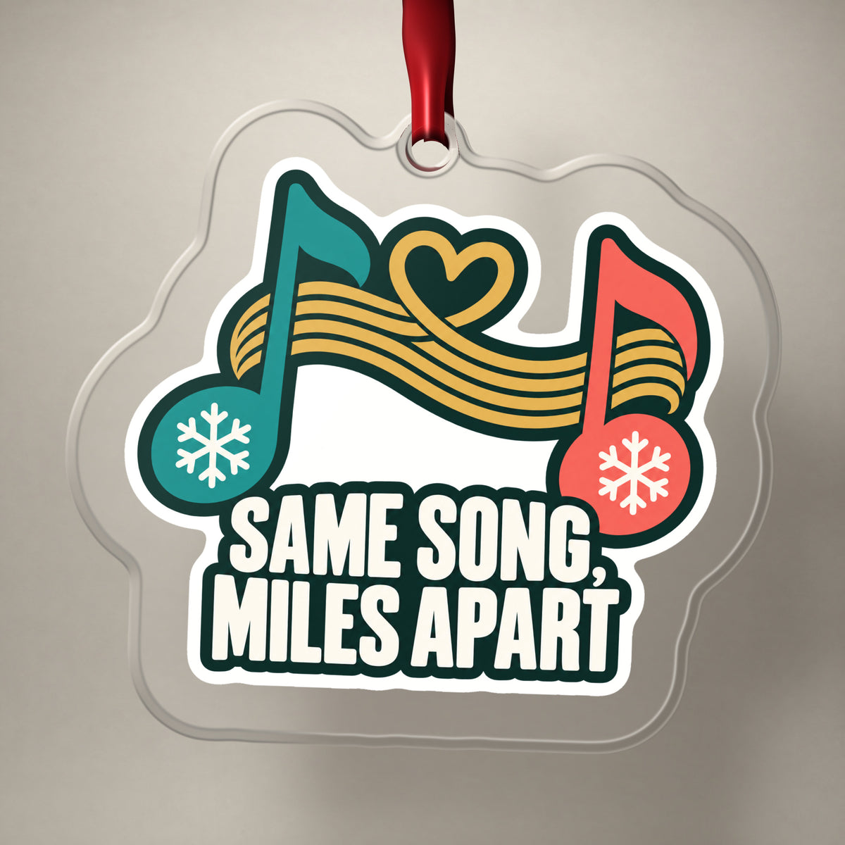 Same Song, Miles Apart Long Distance clear acrylic Christmas ornament on a plain studio backdrop with its red ribbon