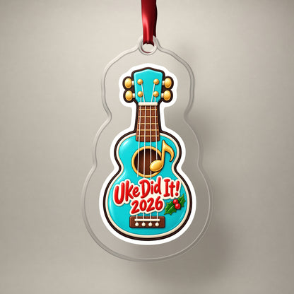 Uke Did It 2026 First Ukulele clear acrylic Christmas ornament on a plain studio backdrop with its red ribbon