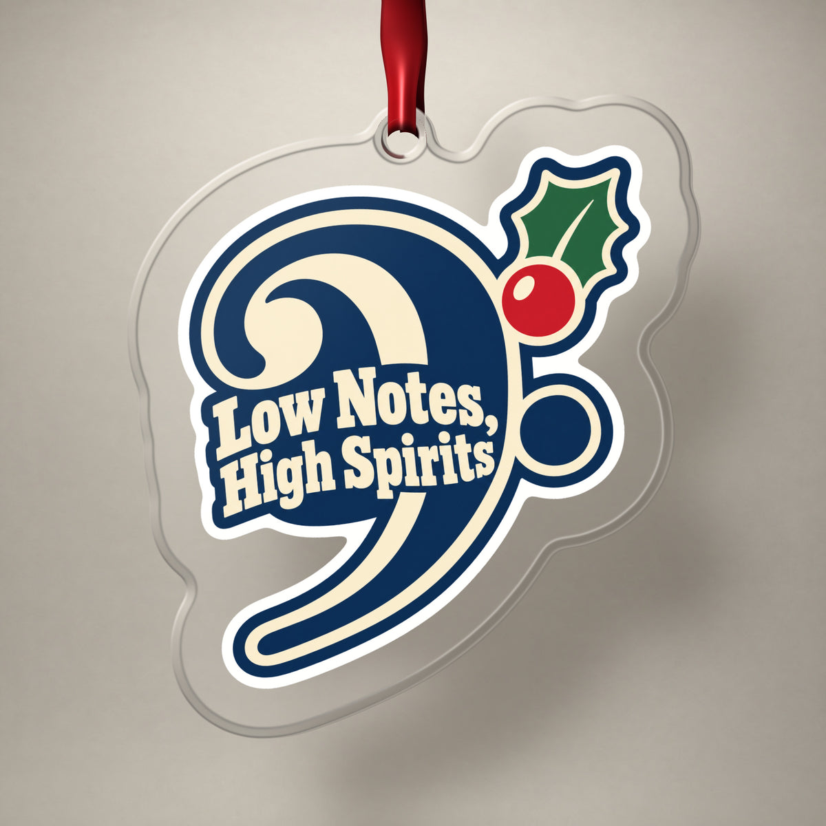 Low Notes, High Spirits Bass Clef clear acrylic Christmas ornament on a plain studio backdrop with its red ribbon