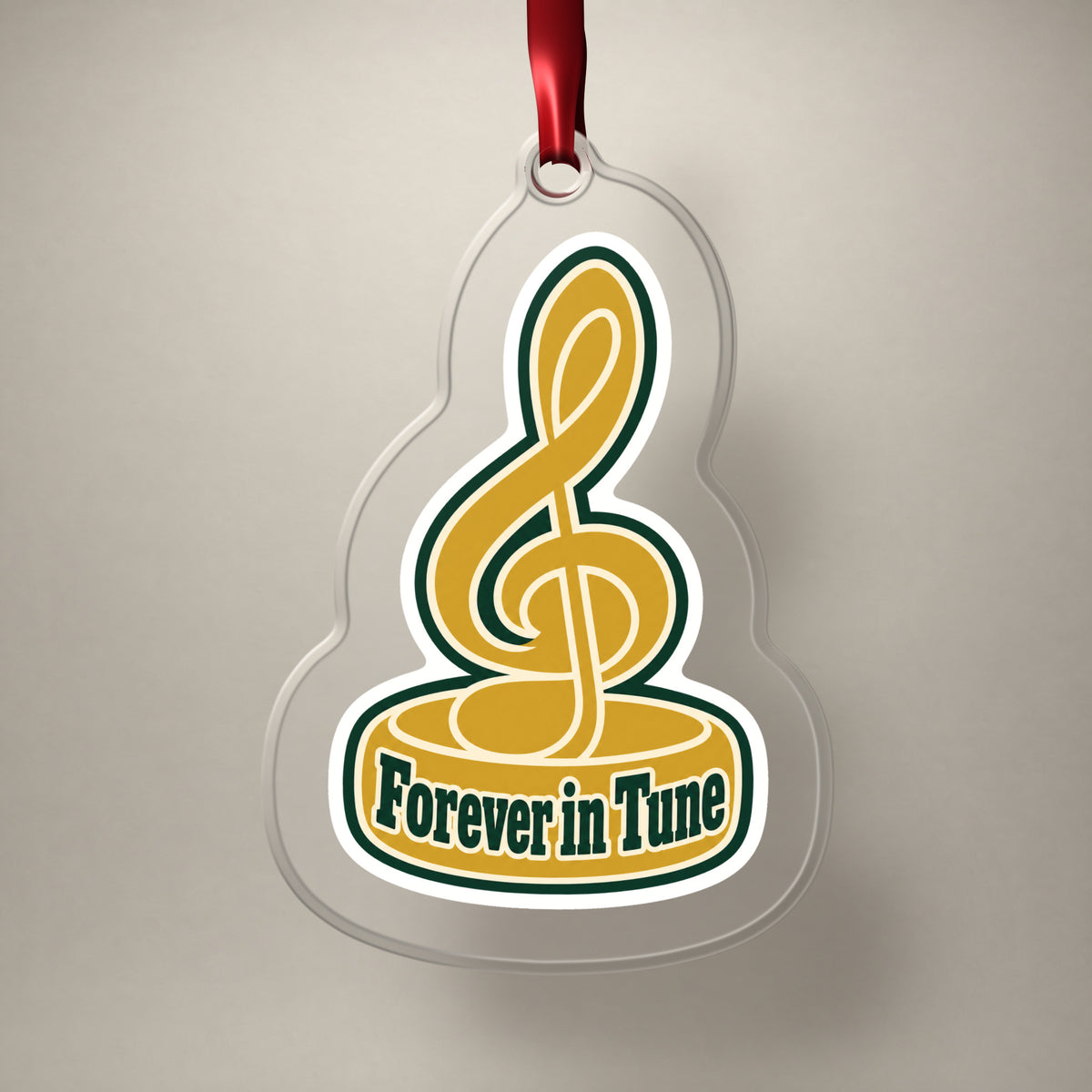 Forever in Tune Treble Clef clear acrylic Christmas ornament on a plain studio backdrop with its red ribbon