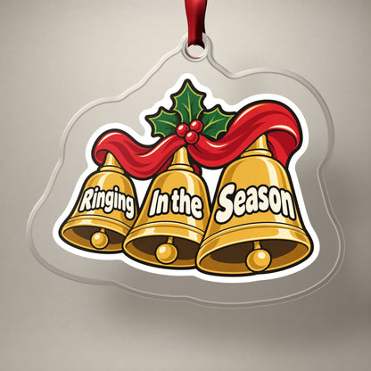Ringing In the Season Handbells clear acrylic Christmas ornament on a plain studio backdrop with its red ribbon