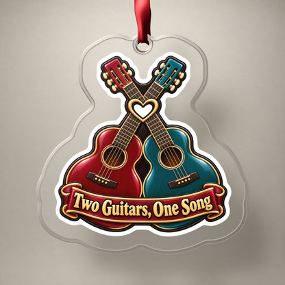 Two Guitars, One Song Couples clear acrylic Christmas ornament on a plain studio backdrop with its red ribbon