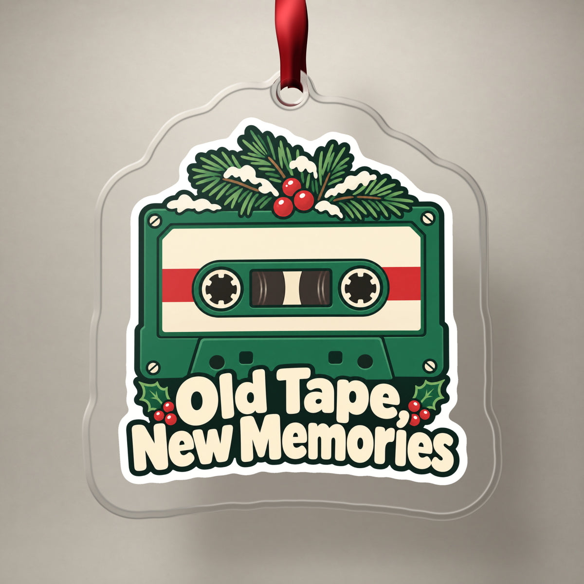 Old Tape, New Memories Cassette clear acrylic Christmas ornament on a plain studio backdrop with its red ribbon