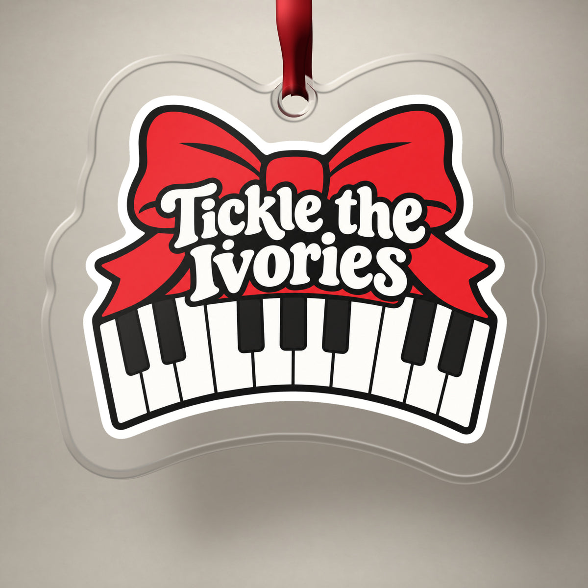 Tickle the Ivories Piano Keys clear acrylic Christmas ornament on a plain studio backdrop with its red ribbon