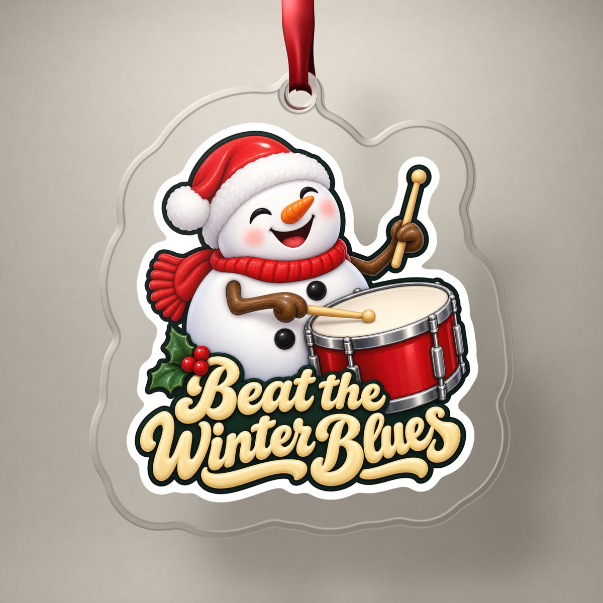 Beat the Winter Blues Snowman Drummer clear acrylic Christmas ornament on a plain studio backdrop with its red ribbon