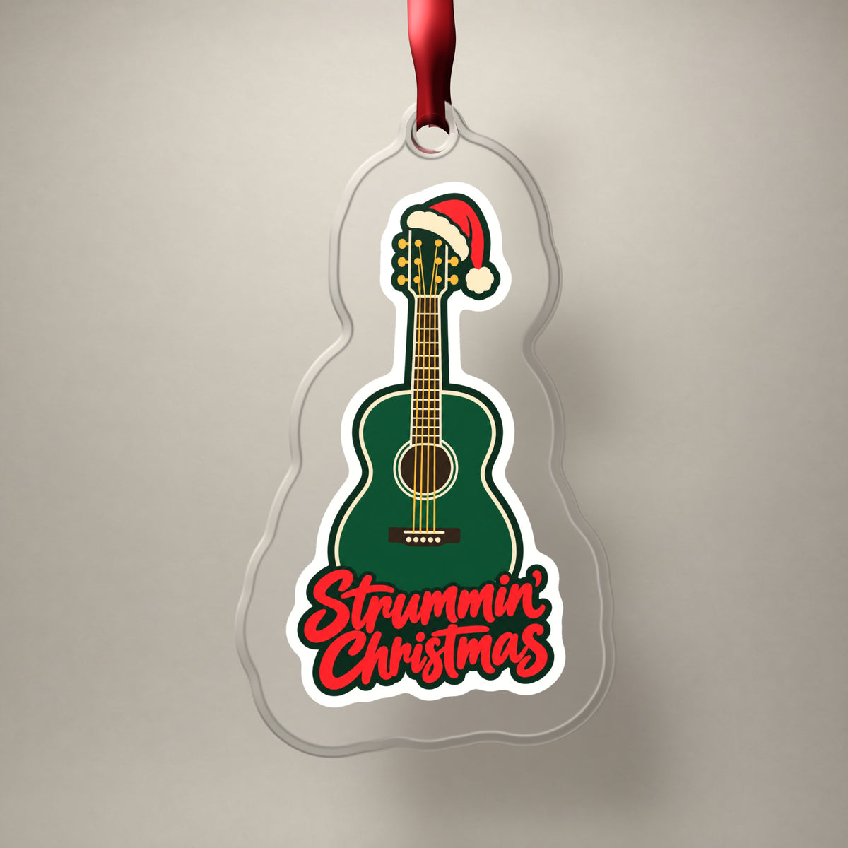 Strummin' Christmas Acoustic Guitar clear acrylic Christmas ornament on a plain studio backdrop with its red ribbon