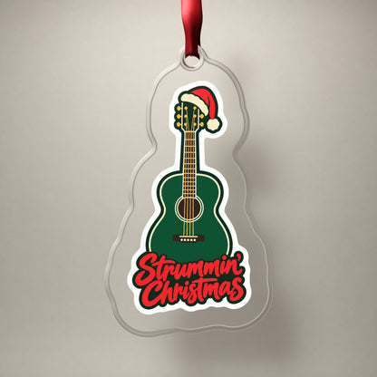 Strummin' Christmas Acoustic Guitar clear acrylic Christmas ornament on a plain studio backdrop with its red ribbon