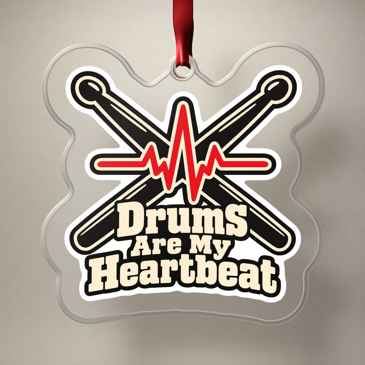Drums Are My Heartbeat Drumsticks clear acrylic Christmas ornament on a plain studio backdrop with its red ribbon