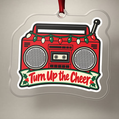 Turn Up the Cheer Boombox clear acrylic Christmas ornament on a plain studio backdrop with its red ribbon