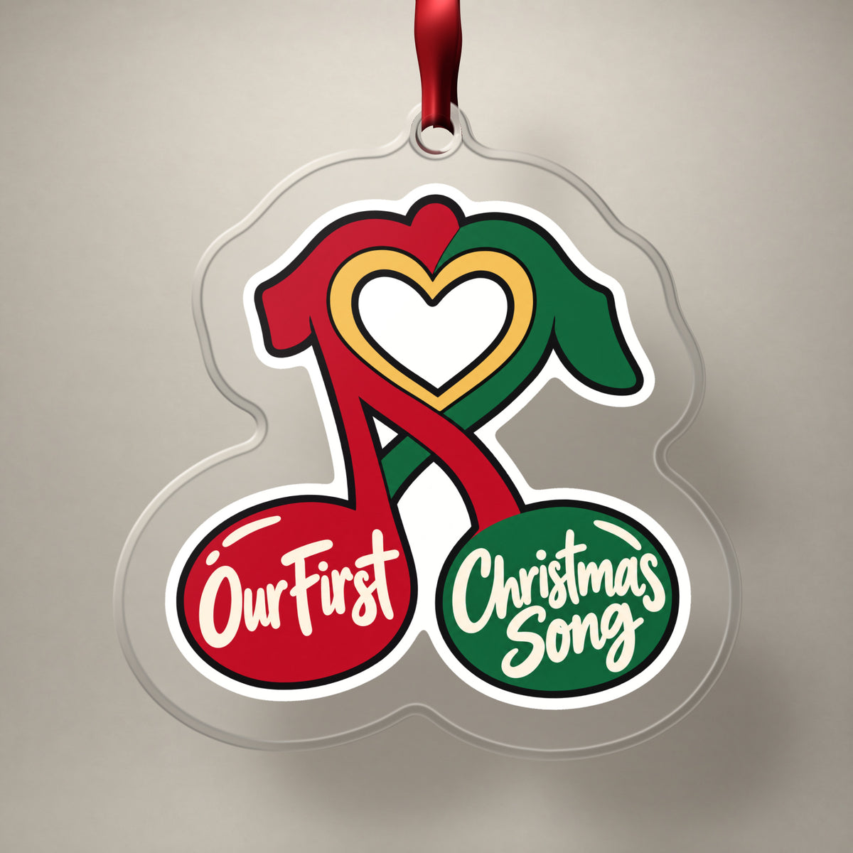 Our First Christmas Song Music Notes clear acrylic Christmas ornament on a plain studio backdrop with its red ribbon