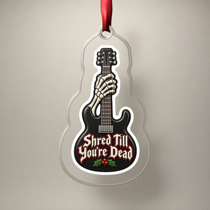 Shred Till You're Dead Skeleton Guitar clear acrylic Christmas ornament on a plain studio backdrop with its red ribbon