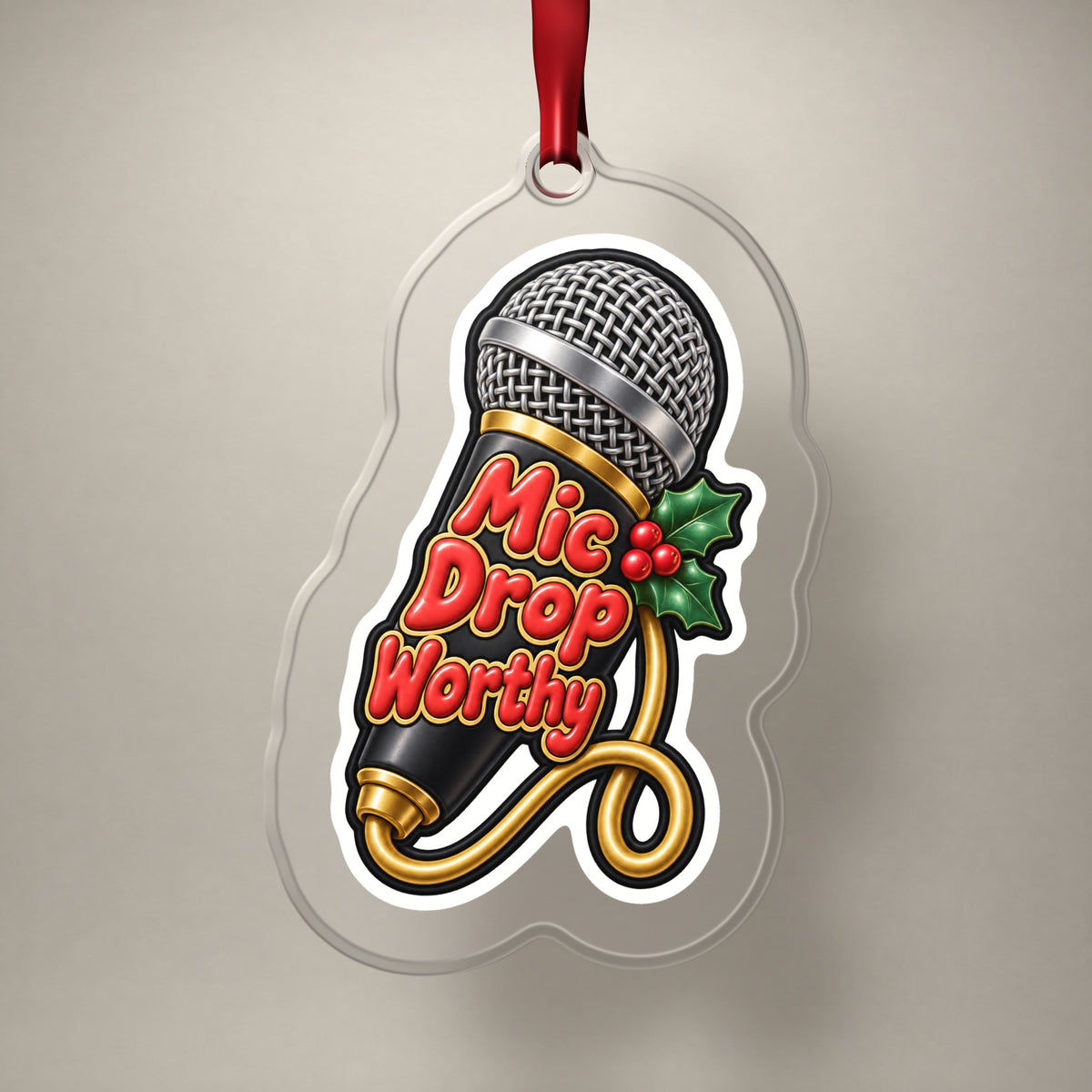 Mic Drop Worthy Microphone clear acrylic Christmas ornament on a plain studio backdrop with its red ribbon