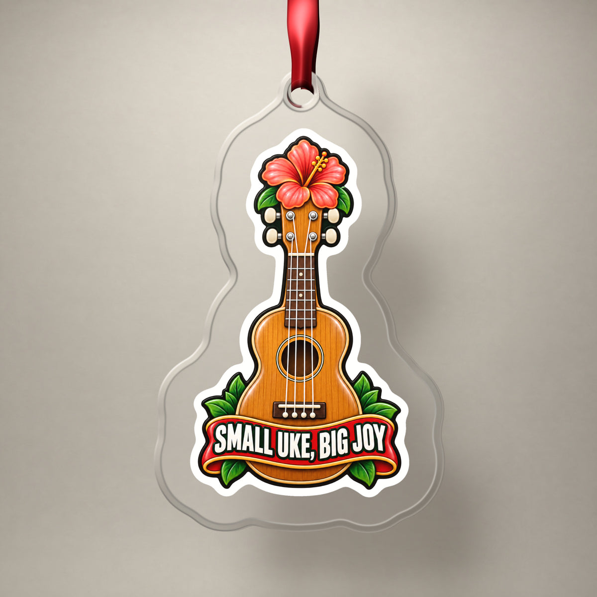 Small Uke, Big Joy Ukulele clear acrylic Christmas ornament on a plain studio backdrop with its red ribbon