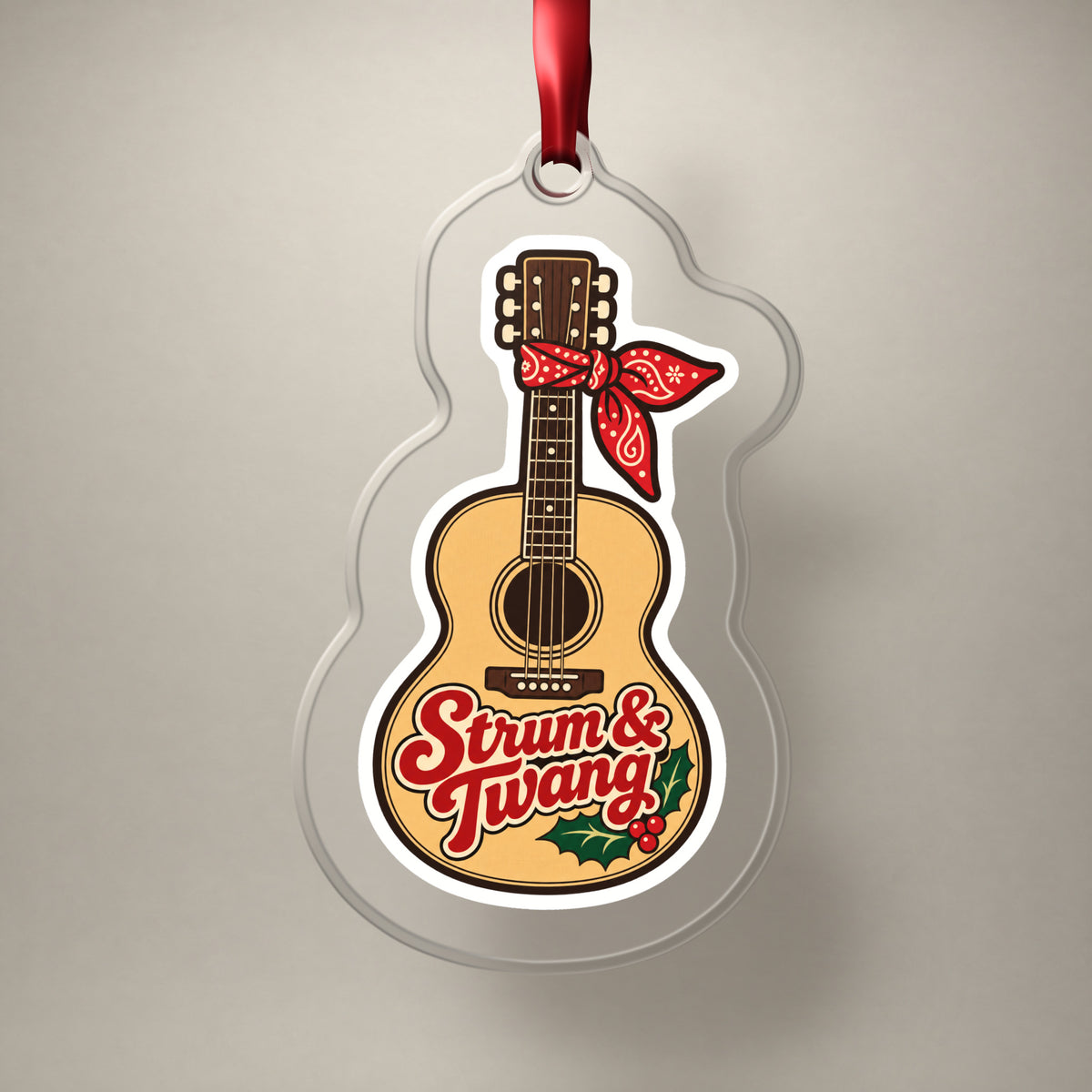 Strum & Twang Country Guitar clear acrylic Christmas ornament on a plain studio backdrop with its red ribbon