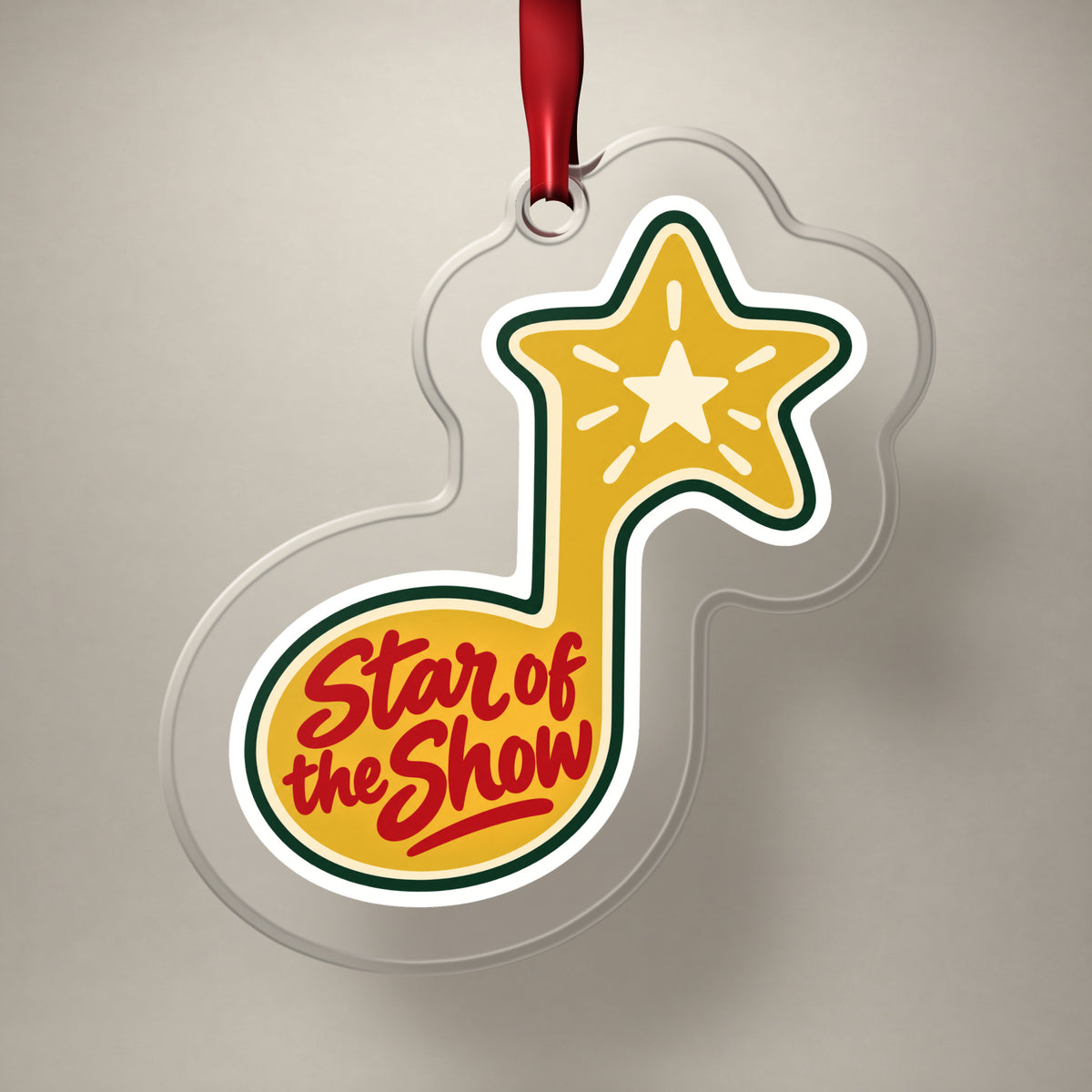Star of the Show Music Note clear acrylic Christmas ornament on a plain studio backdrop with its red ribbon