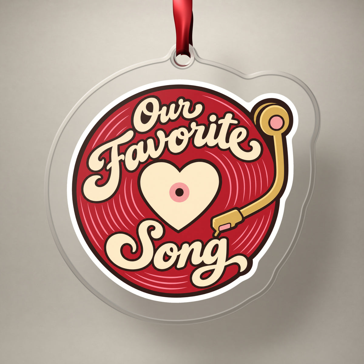 Our Favorite Song Vinyl Record clear acrylic Christmas ornament on a plain studio backdrop with its red ribbon