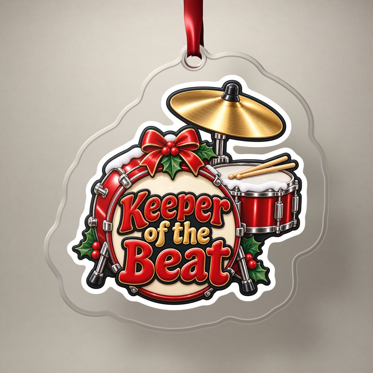 Keeper of the Beat Drum Kit clear acrylic Christmas ornament on a plain studio backdrop with its red ribbon