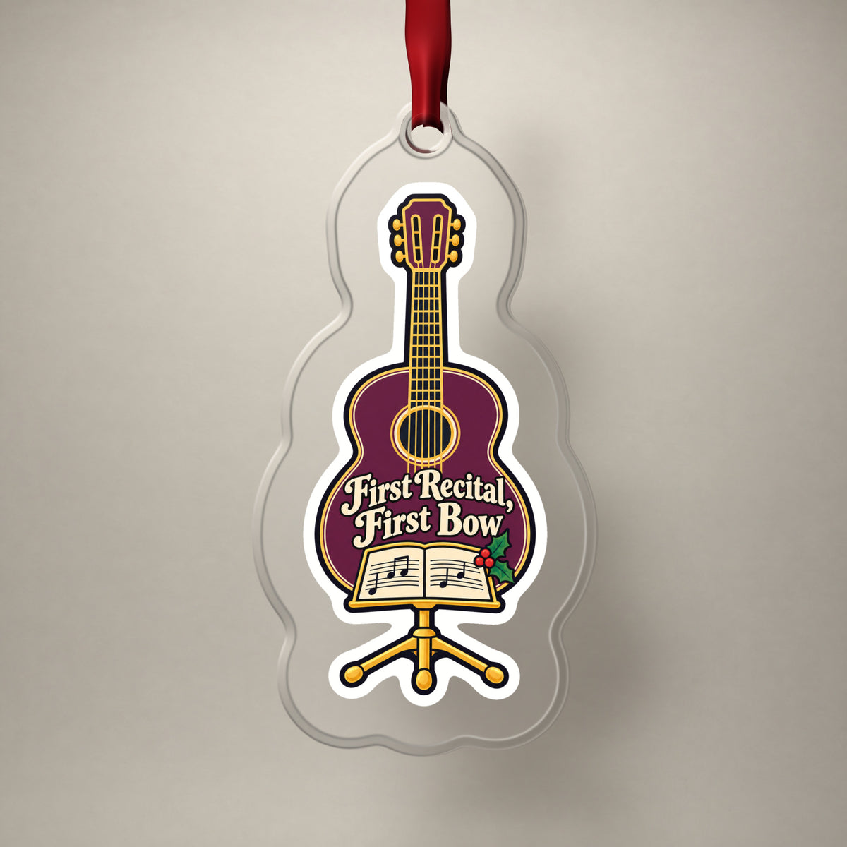 First Recital Acoustic Guitar clear acrylic Christmas ornament on a plain studio backdrop with its red ribbon