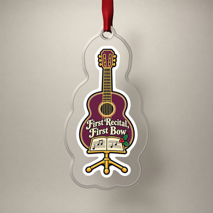First Recital Acoustic Guitar clear acrylic Christmas ornament on a plain studio backdrop with its red ribbon