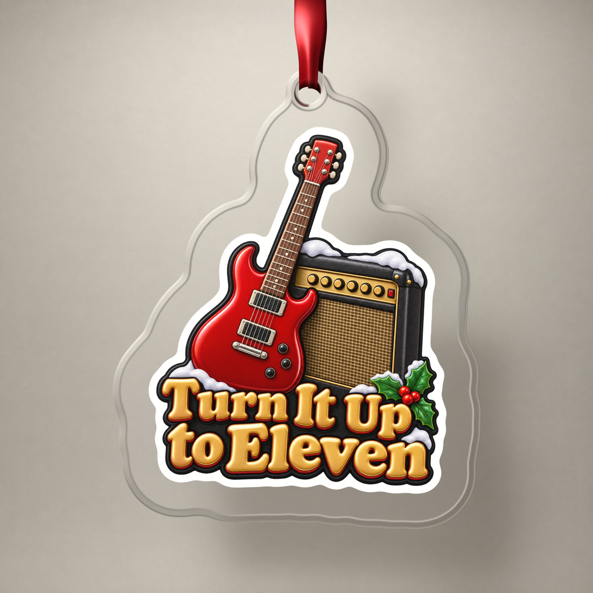 Turn It Up to Eleven Guitar and Amp clear acrylic Christmas ornament on a plain studio backdrop with its red ribbon