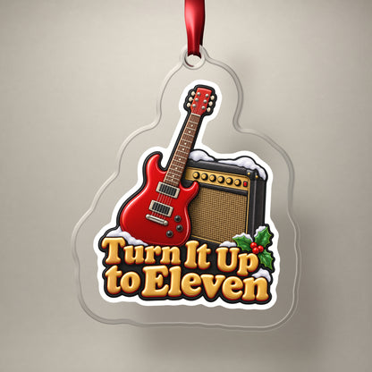 Turn It Up to Eleven Guitar and Amp clear acrylic Christmas ornament on a plain studio backdrop with its red ribbon